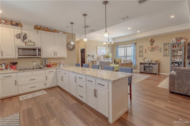 kitchen with stainless steel microwave, open floor plan, a kitchen bar, a tray ceiling, and light wood-style floors