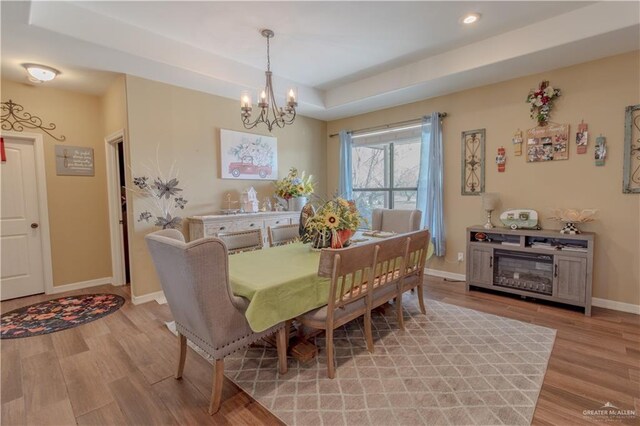 dining room with a chandelier, baseboards, a raised ceiling, and light wood-style floors