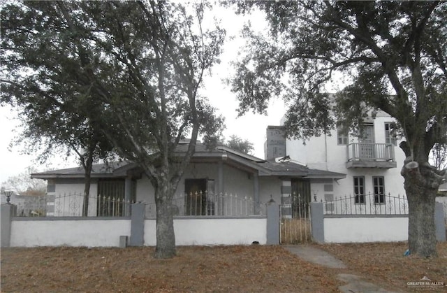 view of front of house with stucco siding, a gate, a fenced front yard, a balcony, and a chimney