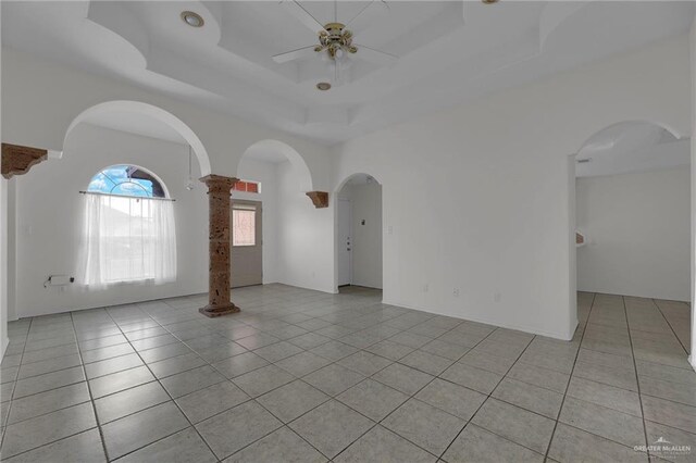 tiled empty room featuring ceiling fan and a raised ceiling