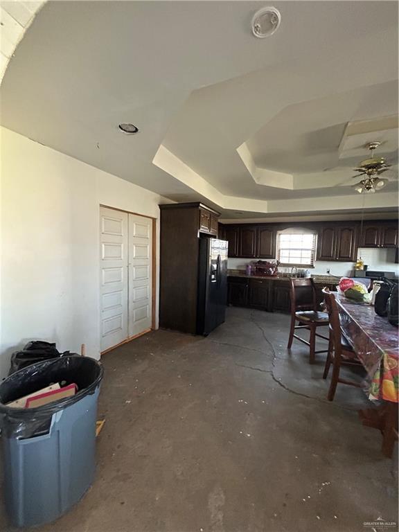 kitchen with ceiling fan, a tray ceiling, concrete flooring, dark brown cabinetry, and fridge with ice dispenser