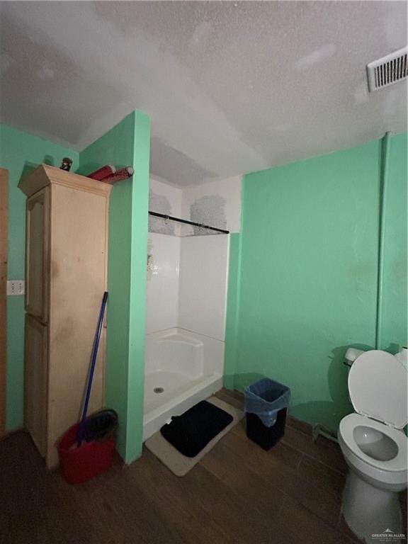 bathroom featuring a shower, a textured ceiling, hardwood / wood-style flooring, and toilet