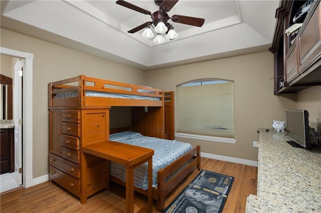 bedroom featuring ceiling fan, light hardwood / wood-style floors, connected bathroom, and a tray ceiling