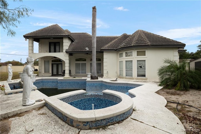 rear view of house featuring ceiling fan and a swimming pool with hot tub