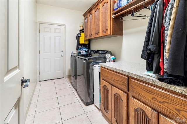 laundry area featuring washing machine and clothes dryer, light tile patterned flooring, and cabinets