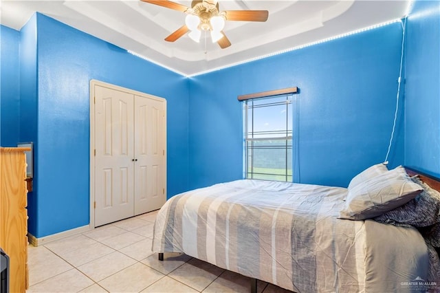 bedroom with a tray ceiling, ceiling fan, a closet, and light tile patterned floors