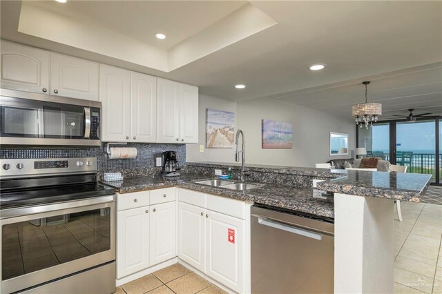 kitchen with stainless steel appliances, a sink, a peninsula, light tile patterned flooring, and white cabinetry