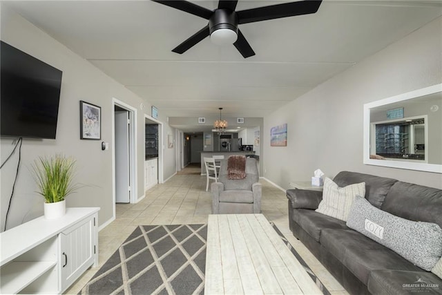 living room featuring light tile patterned floors, ceiling fan, baseboards, and a chandelier
