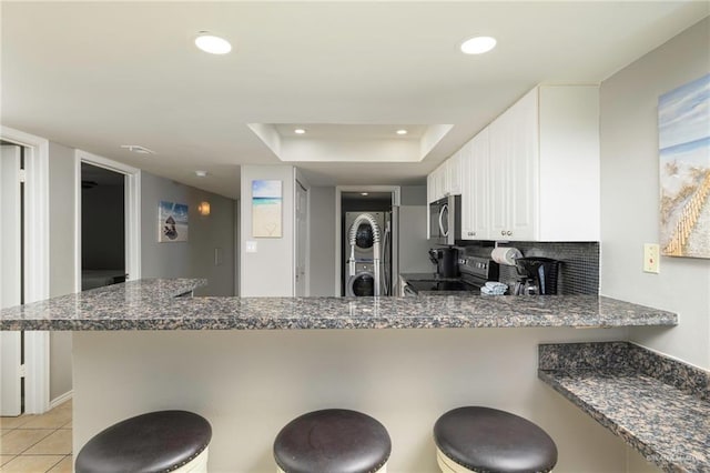 kitchen featuring stacked washer and clothes dryer, appliances with stainless steel finishes, a breakfast bar area, a peninsula, and recessed lighting