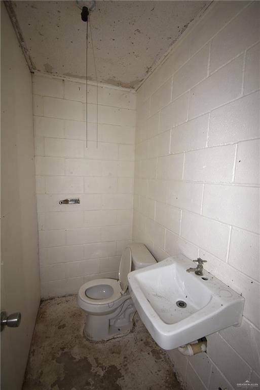 half bath featuring toilet, unfinished concrete floors, concrete block wall, and a sink