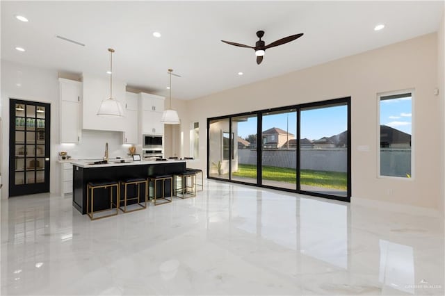 kitchen with plenty of natural light, white cabinets, hanging light fixtures, and a center island with sink