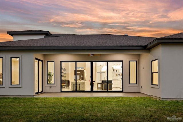 back house at dusk with ceiling fan and a yard