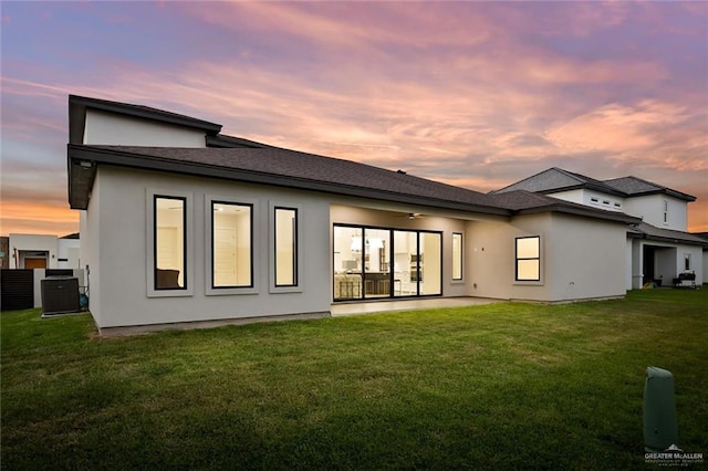 back house at dusk with central AC, ceiling fan, and a lawn