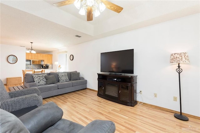 living area with baseboards, a ceiling fan, light wood-style floors, and visible vents