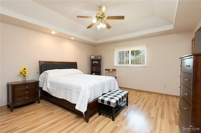 bedroom with a ceiling fan, a tray ceiling, light wood finished floors, baseboards, and recessed lighting