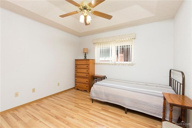 bedroom featuring baseboards, a ceiling fan, a tray ceiling, and wood finished floors