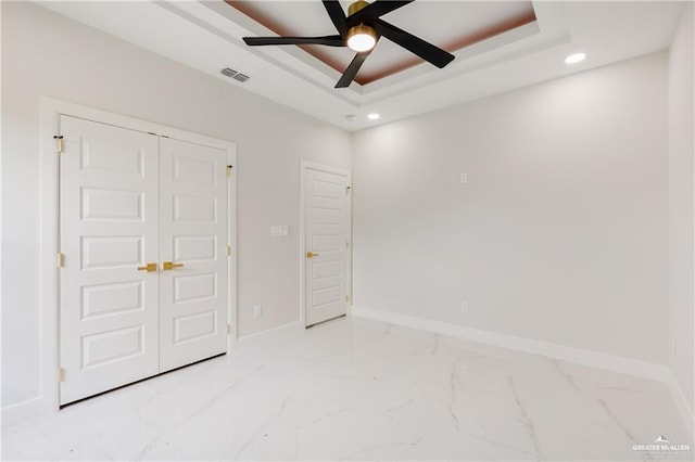 unfurnished bedroom with a tray ceiling, a closet, and ceiling fan