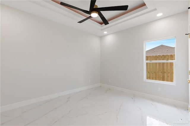 empty room with ceiling fan and a raised ceiling