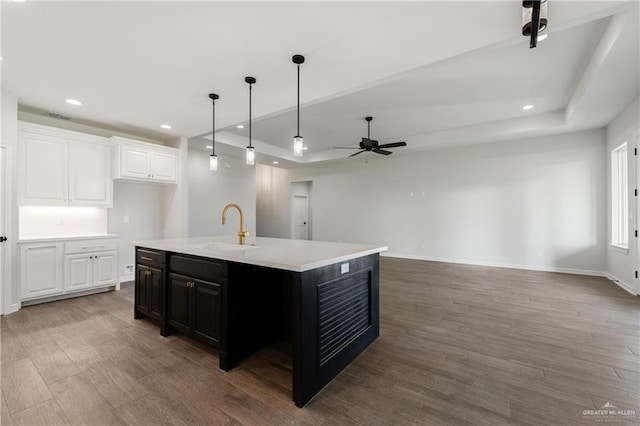 kitchen with hardwood / wood-style floors, a kitchen island with sink, sink, ceiling fan, and white cabinetry