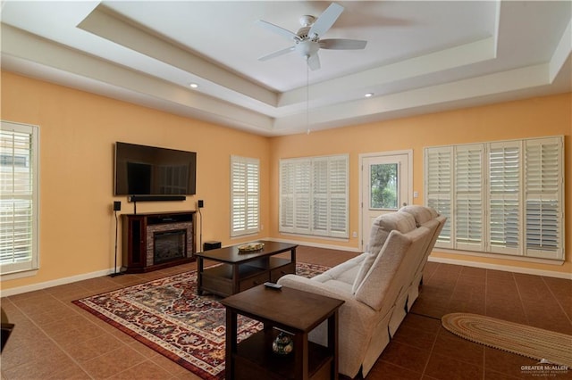 tiled living room with a tray ceiling and ceiling fan