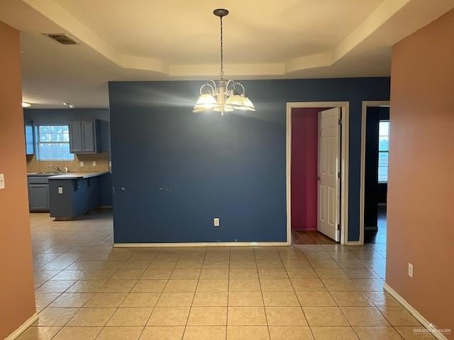 unfurnished dining area with light tile patterned floors, a notable chandelier, and a tray ceiling