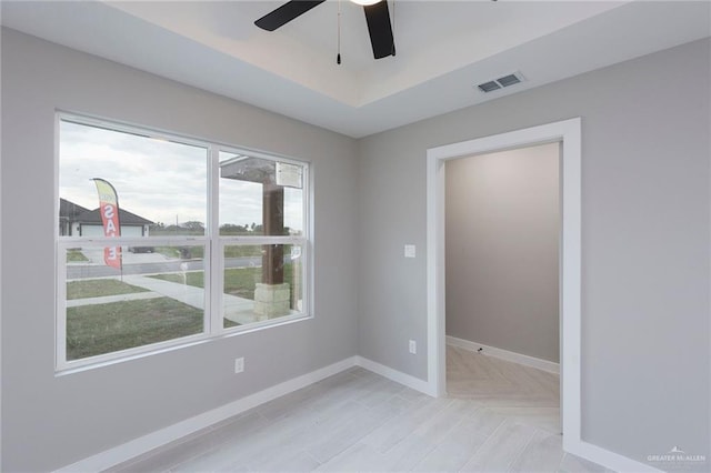 spare room featuring a tray ceiling, ceiling fan, and a healthy amount of sunlight