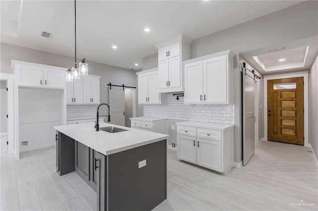 kitchen featuring a barn door, white cabinetry, sink, and an island with sink