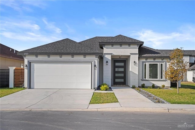 prairie-style house with a shingled roof, concrete driveway, an attached garage, fence, and a front lawn