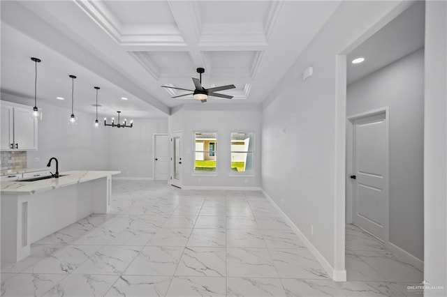 interior space featuring baseboards, coffered ceiling, open floor plan, marble finish floor, and a sink