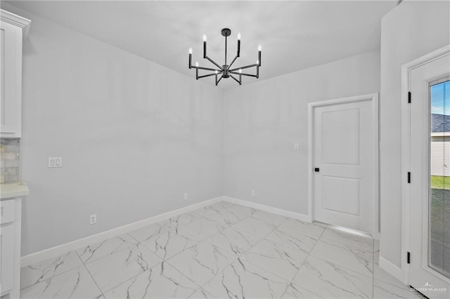 unfurnished dining area featuring marble finish floor, baseboards, and a chandelier