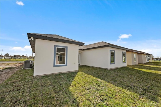 rear view of house with cooling unit, a lawn, and stucco siding