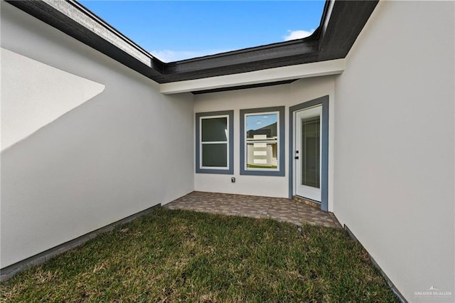 property entrance with a patio area, a yard, and stucco siding