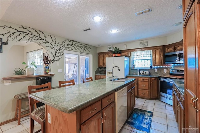 kitchen with a sink, visible vents, a kitchen breakfast bar, appliances with stainless steel finishes, and a center island with sink