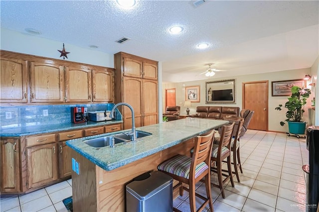 kitchen with light tile patterned floors, a breakfast bar area, a sink, visible vents, and brown cabinets