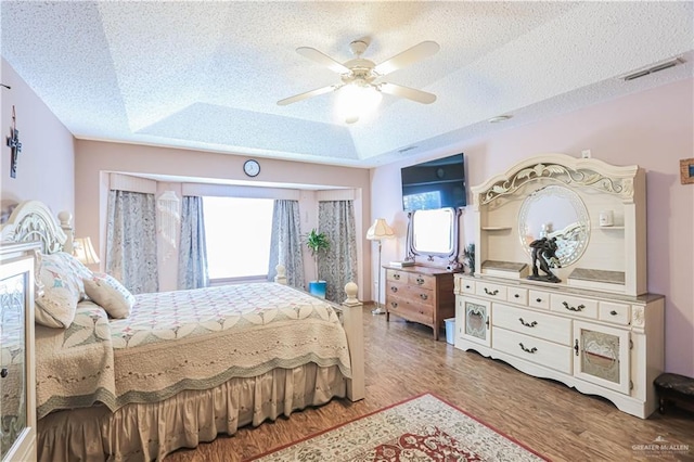 bedroom featuring a textured ceiling, wood finished floors, a raised ceiling, and visible vents