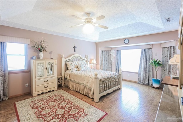 bedroom with a textured ceiling, a ceiling fan, baseboards, light wood-style floors, and a raised ceiling