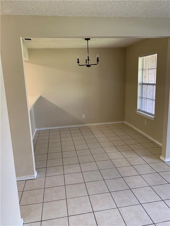 tiled empty room with a chandelier and a textured ceiling