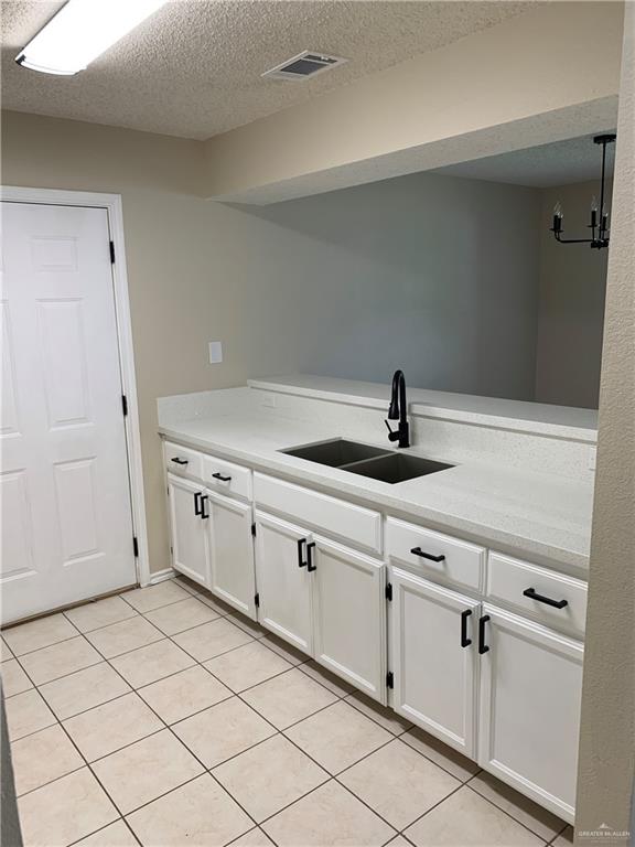 kitchen with white cabinetry, sink, kitchen peninsula, a textured ceiling, and light tile patterned floors