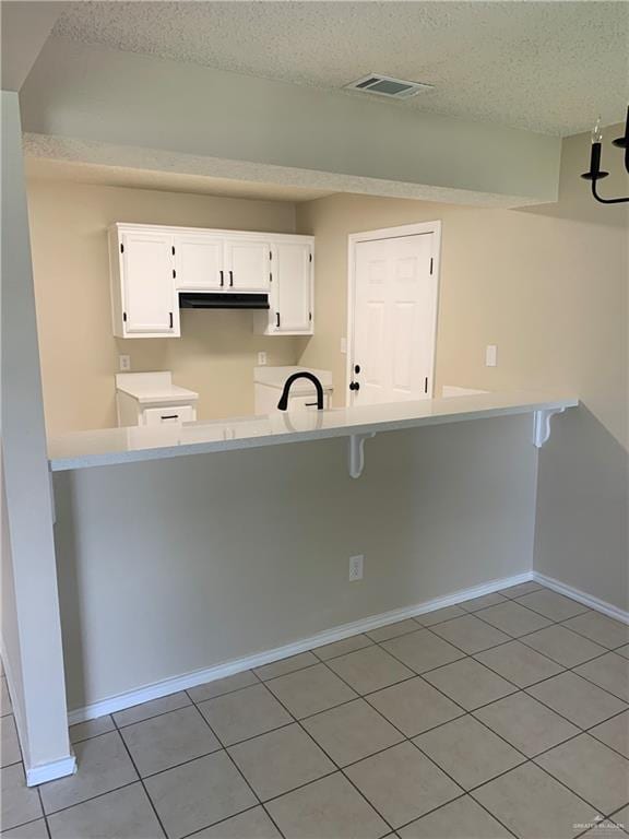 kitchen with white cabinets, a textured ceiling, kitchen peninsula, and light tile patterned flooring