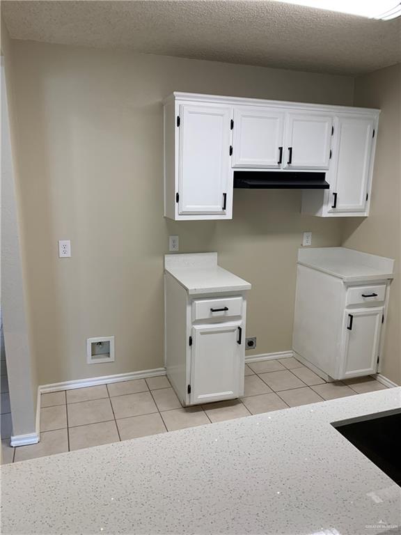 laundry area with electric dryer hookup, light tile patterned floors, cabinets, and a textured ceiling