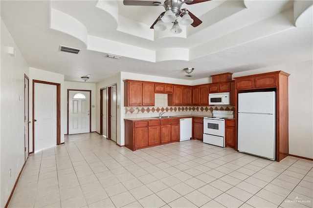 kitchen with ceiling fan, a raised ceiling, white appliances, and backsplash