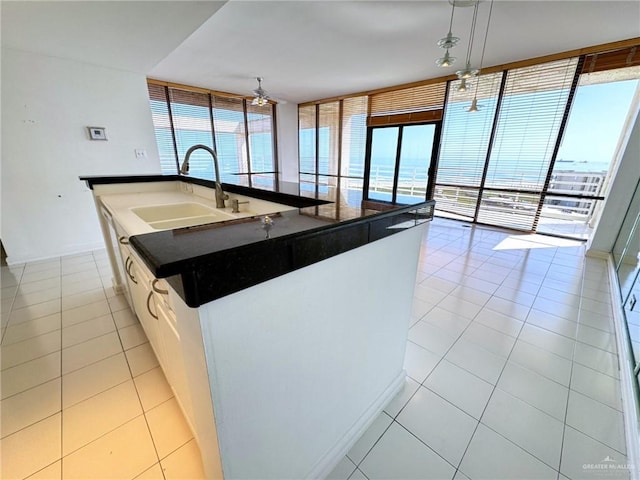 kitchen featuring expansive windows, sink, a center island with sink, pendant lighting, and white cabinets