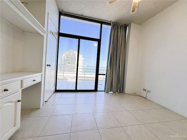 spare room with light tile patterned floors, expansive windows, a textured ceiling, and ceiling fan