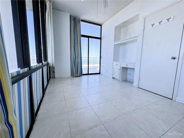 spare room with a wall of windows, built in desk, a textured ceiling, light tile patterned flooring, and built in shelves