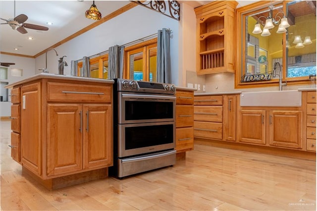 kitchen featuring hanging light fixtures, crown molding, sink, stainless steel stove, and light hardwood / wood-style floors