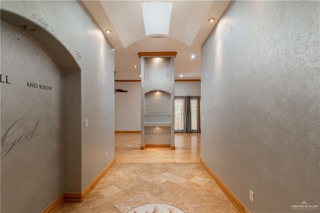 corridor with light hardwood / wood-style floors, lofted ceiling with skylight, and ornamental molding