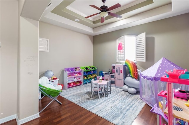 rec room with a tray ceiling, ceiling fan, crown molding, and wood-type flooring