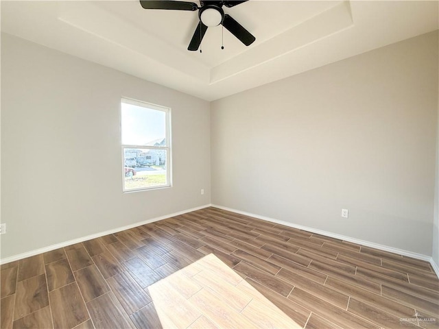 unfurnished room with ceiling fan, a raised ceiling, and wood-type flooring