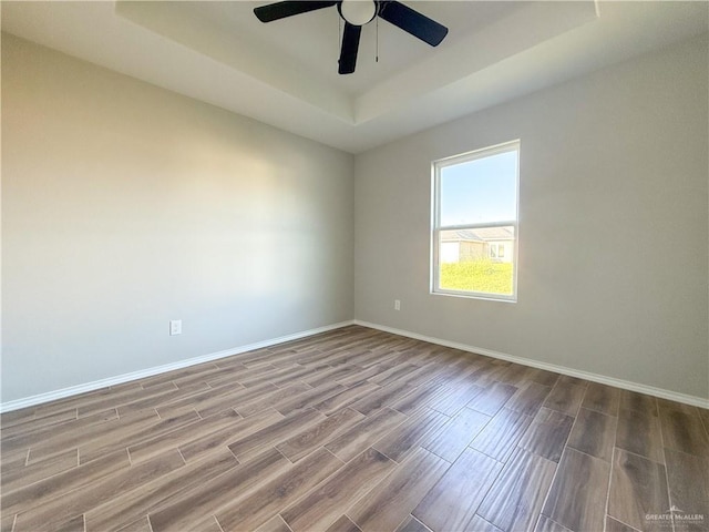 empty room featuring wood-type flooring, a raised ceiling, and ceiling fan