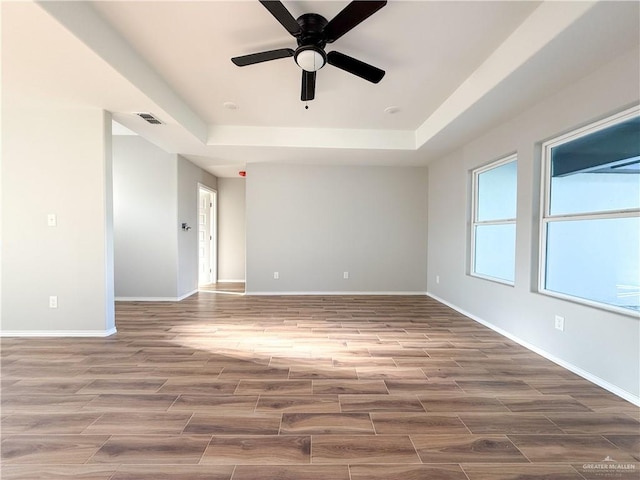 empty room featuring hardwood / wood-style floors, ceiling fan, and a raised ceiling